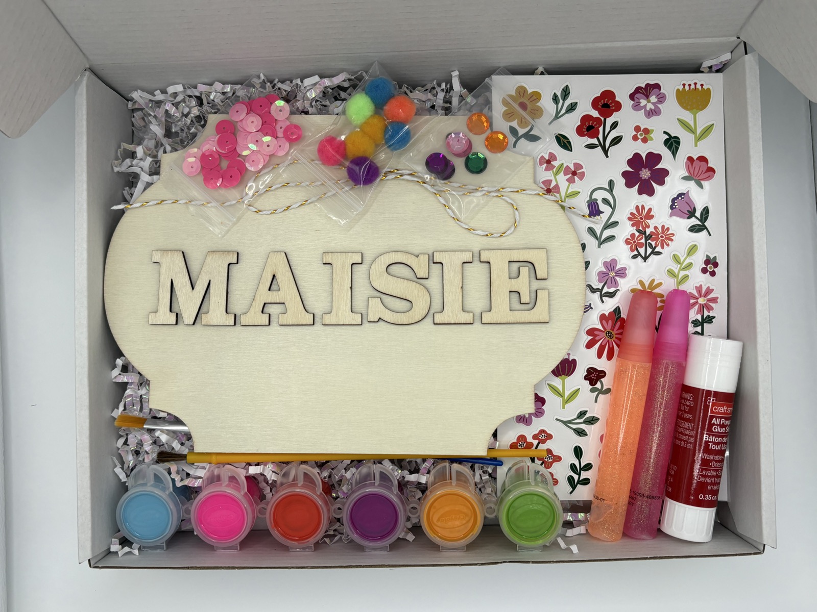 Open personalized floral name-sign craft kit with bright paints, sequins, pom-poms, glitter glue, and flower stickers